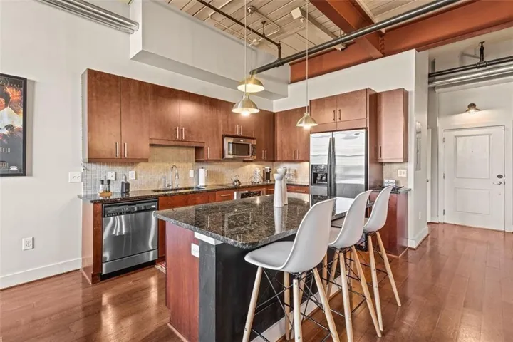Kitchen featuring wood-finish flooring, stainless steel appliances, dark stone countertops, and wood cabinetry
