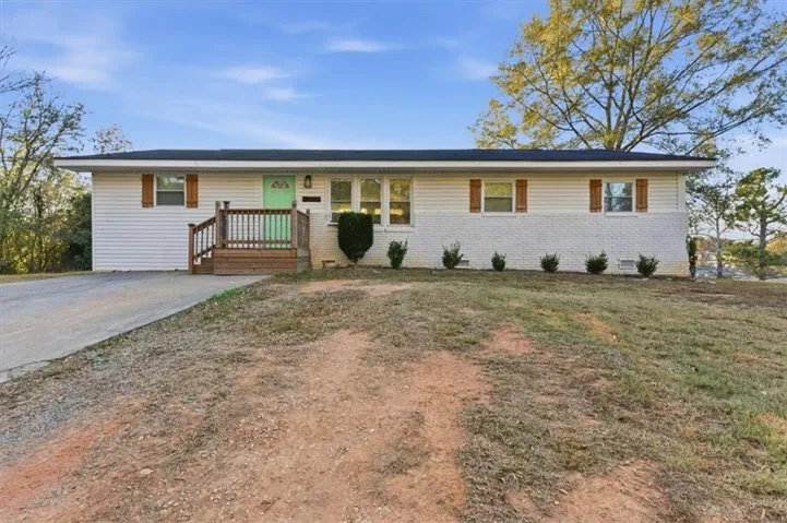 Ranch-style residence featuring white siding and painted brick, a front porch with natural wood railings, a vibrant front door, and wooden window shutters