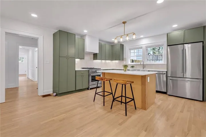 Contemporary kitchen featuring light wood-finish flooring, sage green cabinetry, a central island with a white quartz countertop, and stainless steel appliances