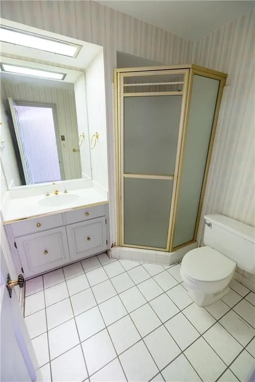 Bathroom featuring wallpapered walls, light tile patterned flooring, vanity, and a shower stall