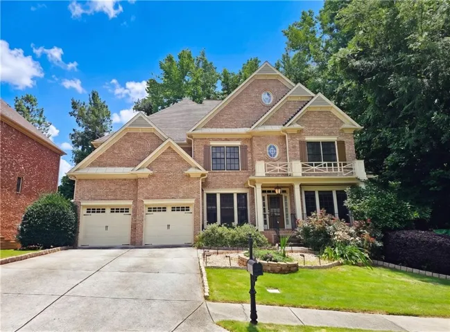 Brick exterior architecture featuring a two-car garage with carriage-style doors, a covered porch entry, upper-level balcony, and gabled rooflines