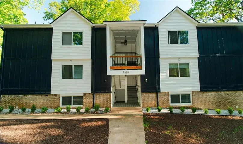 Two-story exterior with white siding and dark panels, brick foundation, and a central covered entrance with a second-story balcony