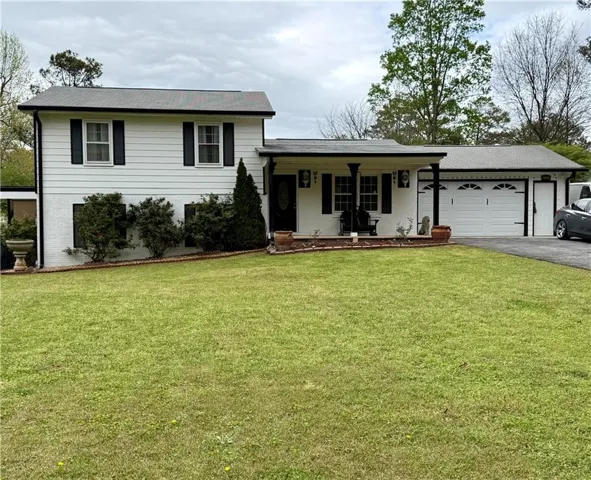 Tri-level home with covered porch, asphalt driveway, a front lawn, and an attached garage