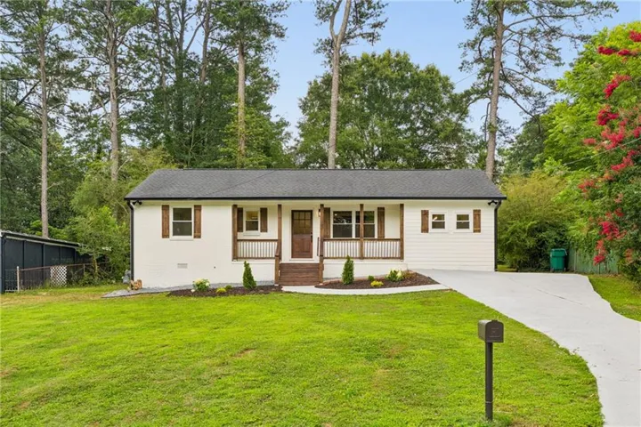 White facade with dark trim, front porch with wood railing, dark wood front door, manicured lawn, and paved driveway