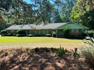 Brick exterior with light green shutters, a gray shingle roof, and a mature tree canopy