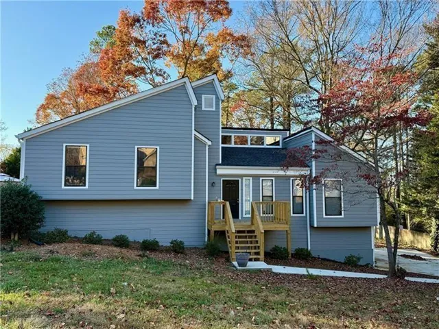 Modern two-story residence featuring light blue fiber cement siding, multi-pane windows, and a covered front entry with wooden deck stairs