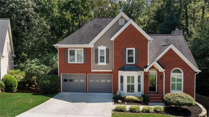 Brick and siding exterior with a dark shingle roof, featuring a two-car garage with gray doors, a bay window, and an arched entry