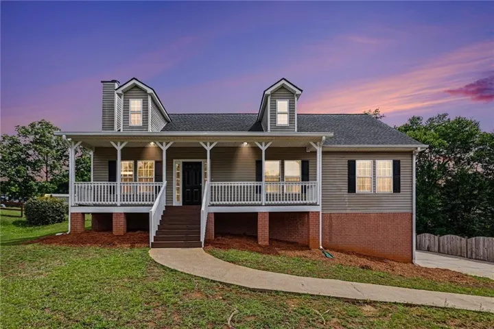 Traditional-style home featuring a covered front porch with white railing, dormer windows, a dark shingle roof, and a visible foundation with brick accents
