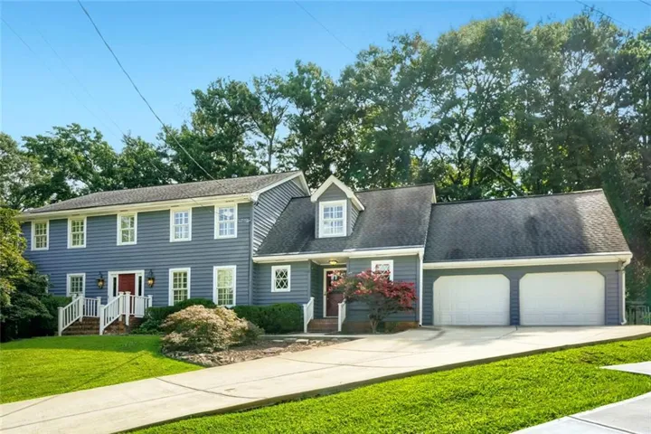 Traditional style residence featuring blue fiber cement siding with white trim, a prominent front-facing garage with two white panel doors, a peaked roof with dormers, and a welcoming covered entry