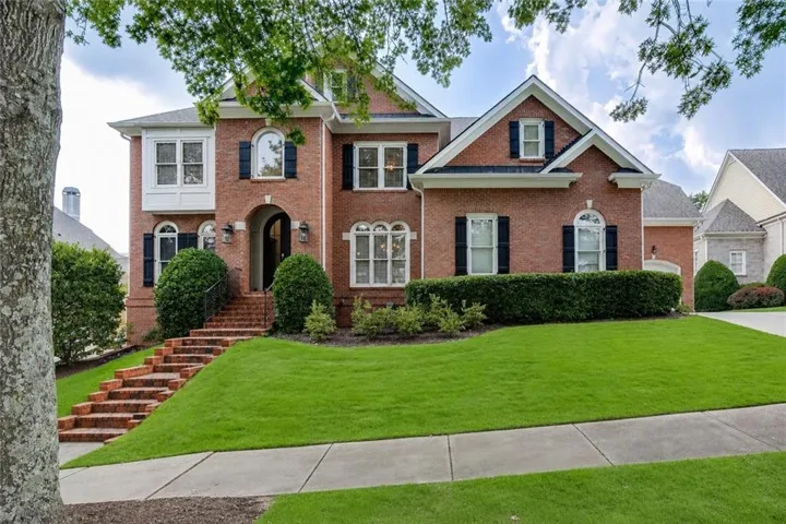 Brick exterior with a prominent arched entry, framed by mature trees and manicured landscaping