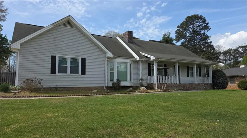 View of front of home with a porch, a front yard, a chimney, and roof with shingles