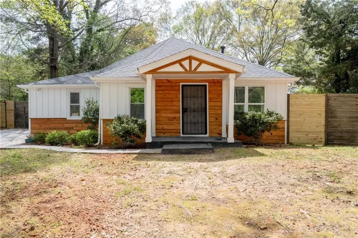 Exterior featuring white vertical siding, wood horizontal siding, a covered porch with decorative wood gable, and a dark grey shingle roof