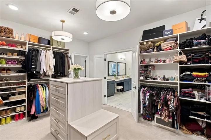 Spacious custom closet featuring a central island with drawers, integrated seating, extensive built-in shelving, multiple hanging rods, and recessed lighting - primary closet