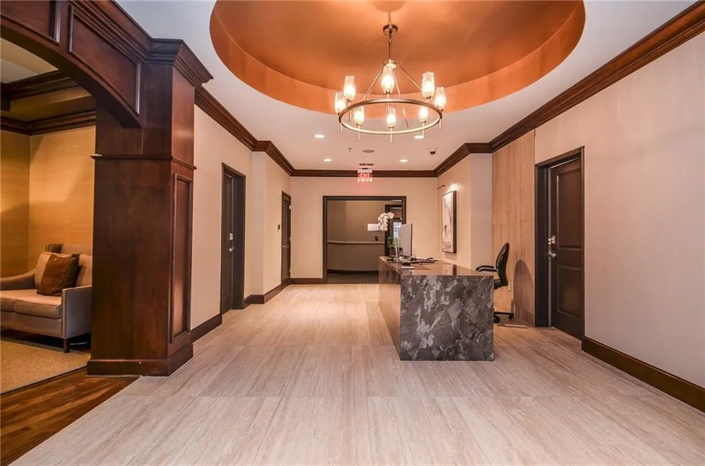 Hall with light hardwood / wood-style flooring, a chandelier, a raised ceiling, and ornamental molding