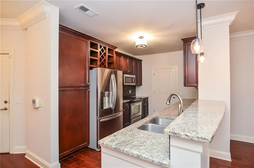 Kitchen featuring pendant lighting, sink, kitchen peninsula, appliances with stainless steel finishes, and dark hardwood / wood-style flooring