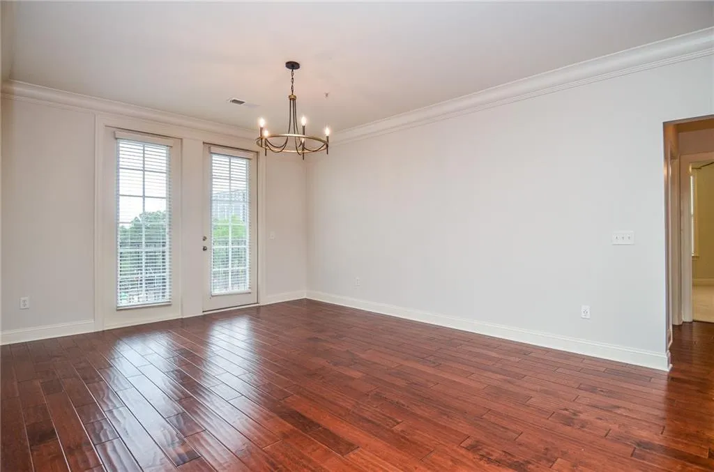 Empty room featuring crown molding, dark hardwood / wood-style flooring, and a notable chandelier