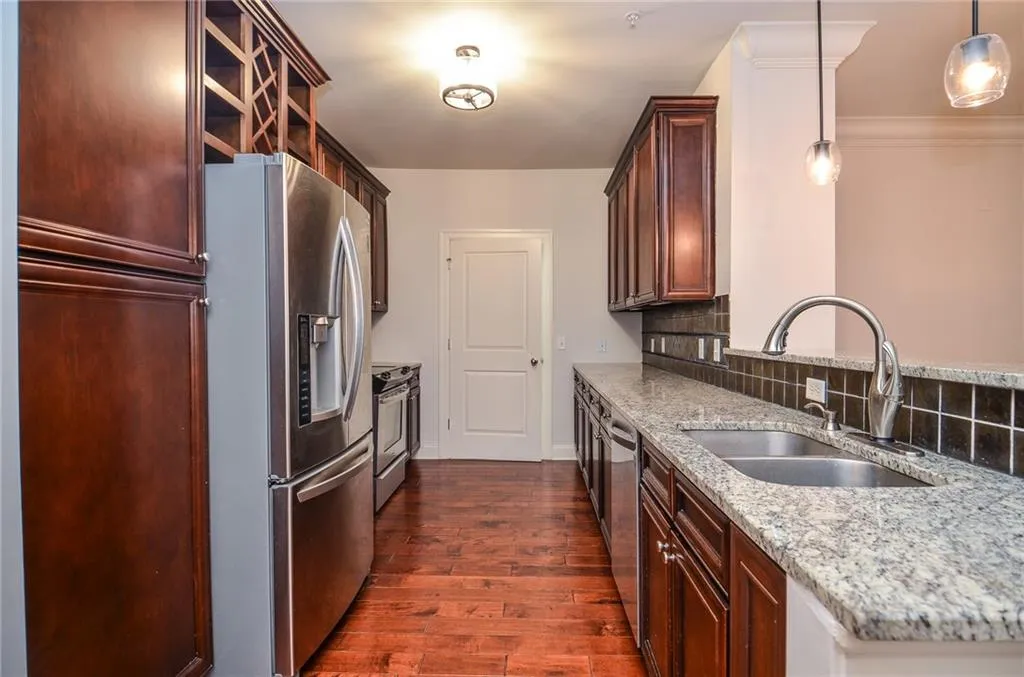 Kitchen with pendant lighting, backsplash, appliances with stainless steel finishes, dark hardwood / wood-style floors, and light stone countertops