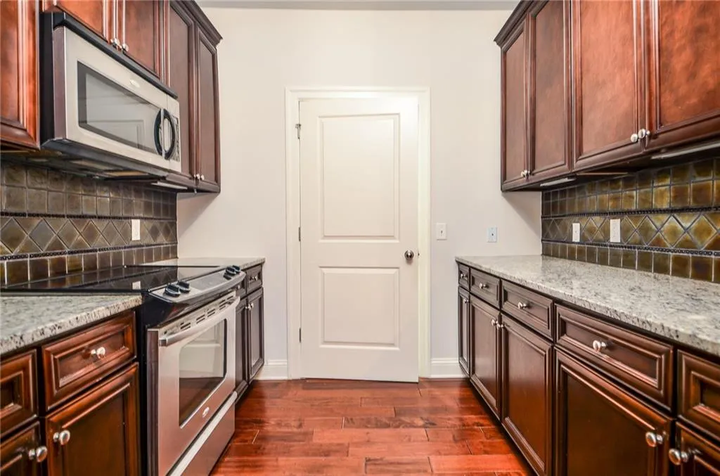 Kitchen with appliances with stainless steel finishes, decorative backsplash, dark hardwood / wood-style flooring, and light stone counters
