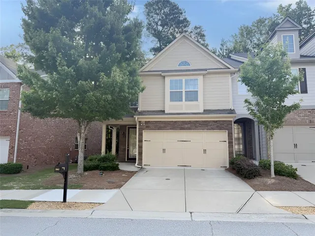 Elegant two-story home featuring a cream-colored exterior with architectural detailing, two-car garage with paneled doors, and a circular driveway