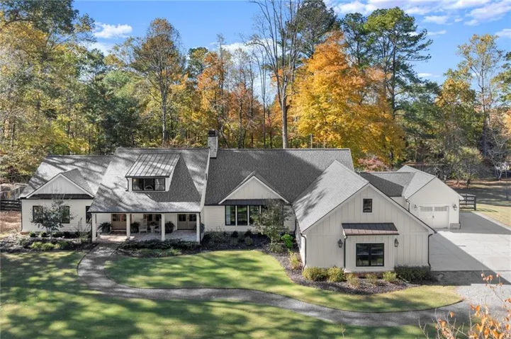 White board and batten exterior with black-framed windows, a covered front porch, an attached two-car garage, an asphalt driveway, and a shingle roof