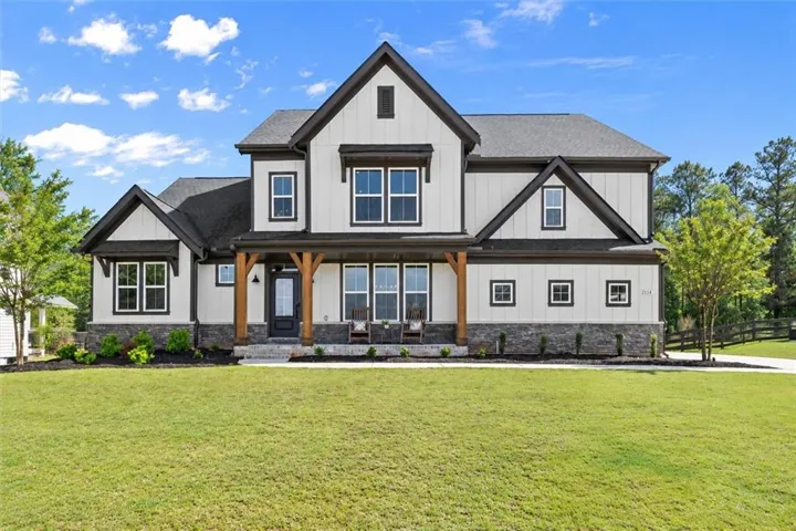 Modern farmhouse exterior with board and batten siding, dark trim accents, stone veneer foundation, a covered porch with timber columns, and a paved driveway