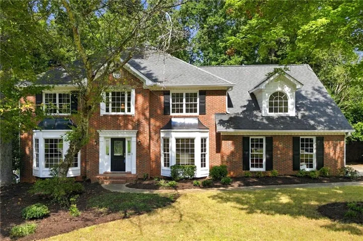 Brick exterior with multiple bay windows, black shutters, and a prominent front entry