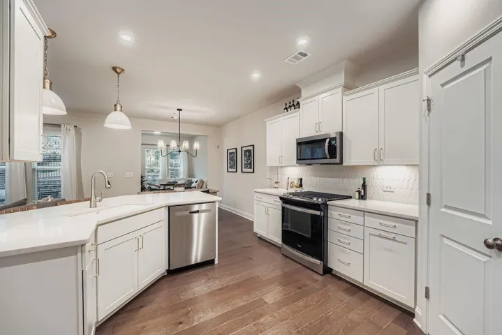 Modern kitchen featuring white shaker cabinetry, stainless steel appliances, light-toned countertops, a textured backsplash, and wood-finish flooring