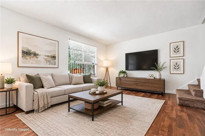 White walls, wood-finish flooring, staircase with carpeted treads, window with horizontal blinds, built-in media console