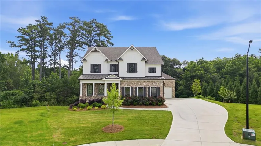 Modern farmhouse exterior featuring white siding with dark window shutters, stone veneer accents, a dark shingle roof, and a two-car garage