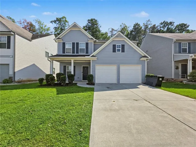 Two-story residence featuring light blue siding with white trim, a covered front porch, and a two-car garage with white doors