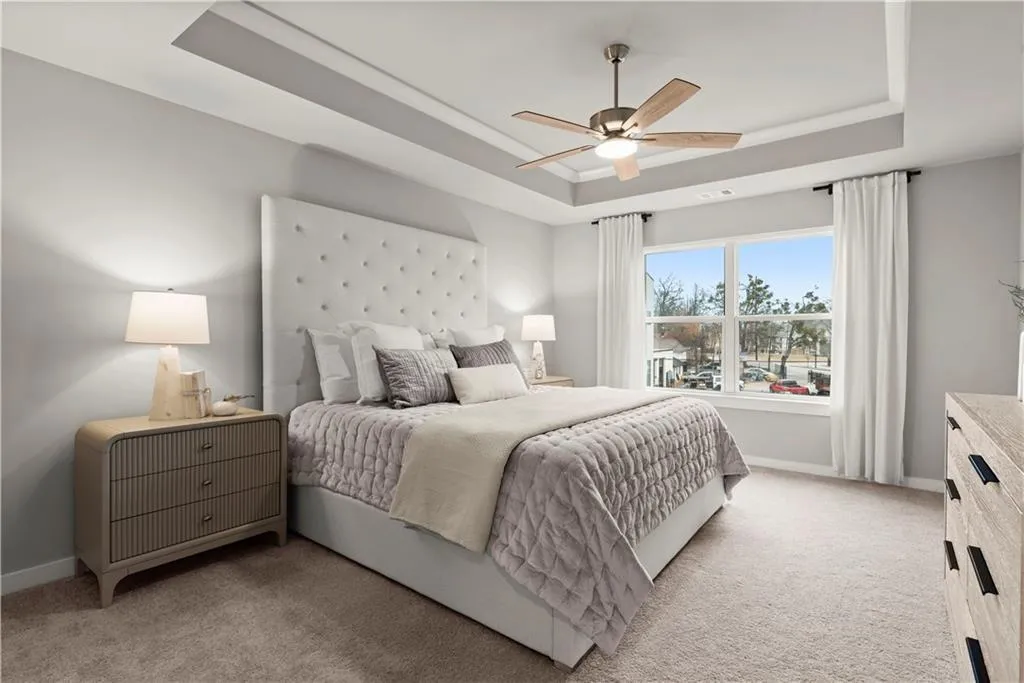 Bedroom featuring a raised ceiling, light carpet, and ceiling fan
