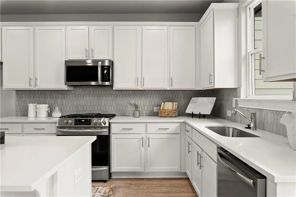 Kitchen featuring white cabinetry, stainless steel appliances, light wood-style floors, light stone counters, and decorative backsplash