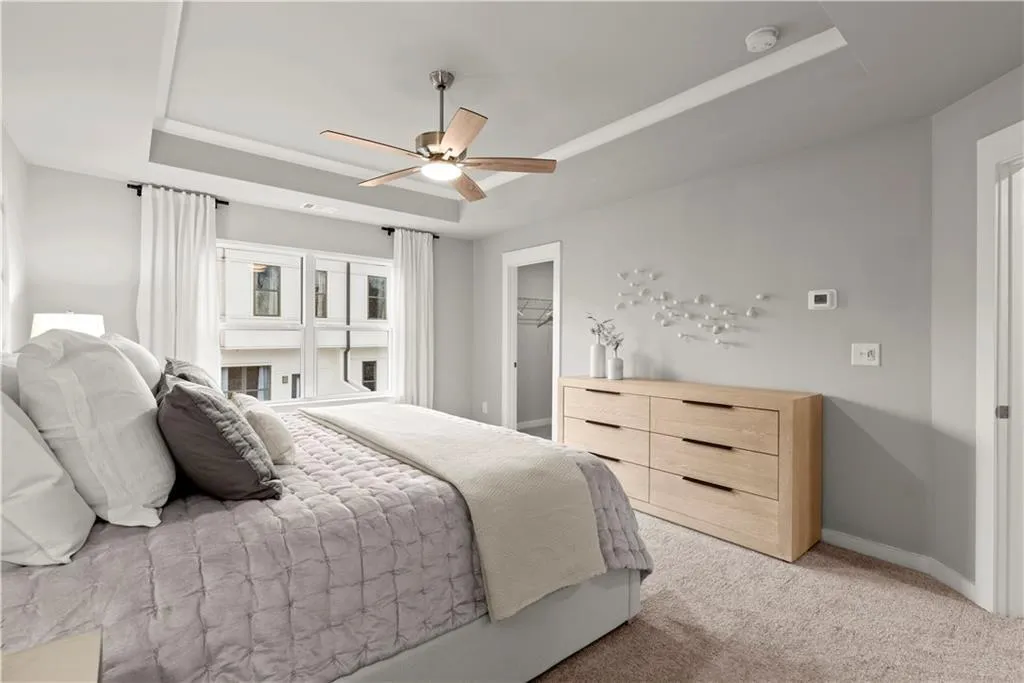 Bedroom with a raised ceiling, light colored carpet, a ceiling fan, and a walk in closet