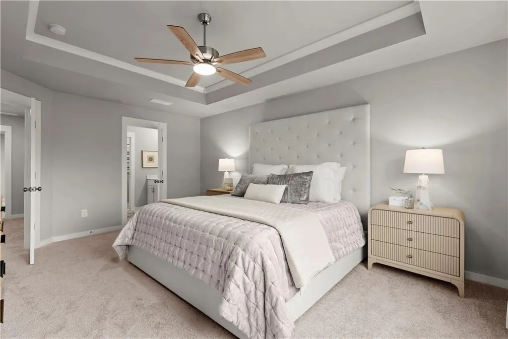 Carpeted bedroom with a raised ceiling, a ceiling fan, and connected bathroom