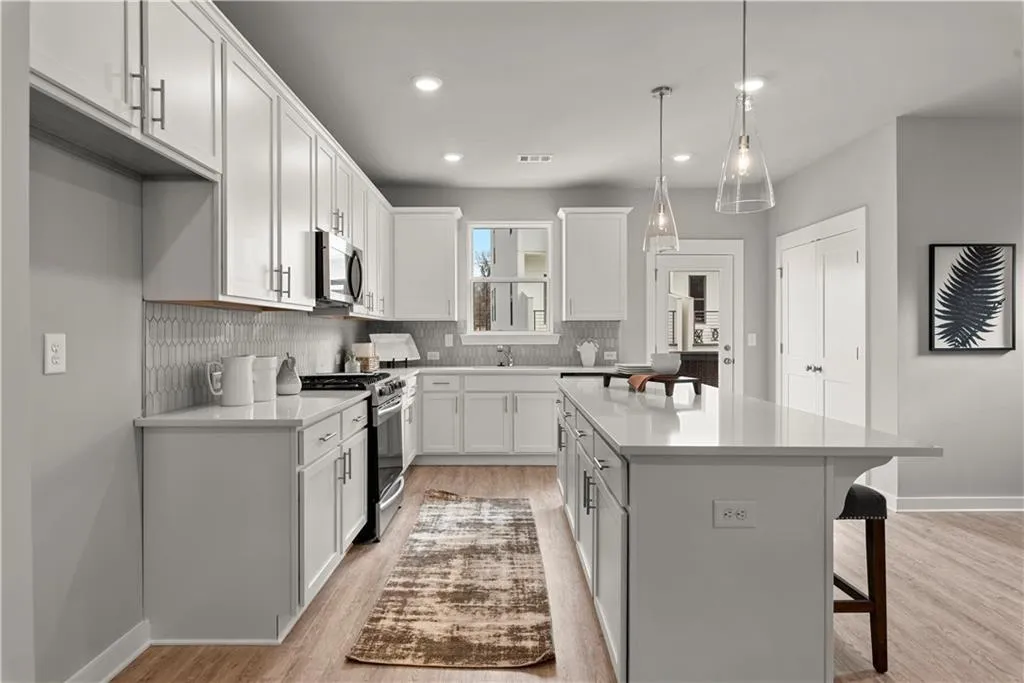 Kitchen with a kitchen breakfast bar, light wood-style flooring, appliances with stainless steel finishes, hanging light fixtures, and white cabinetry