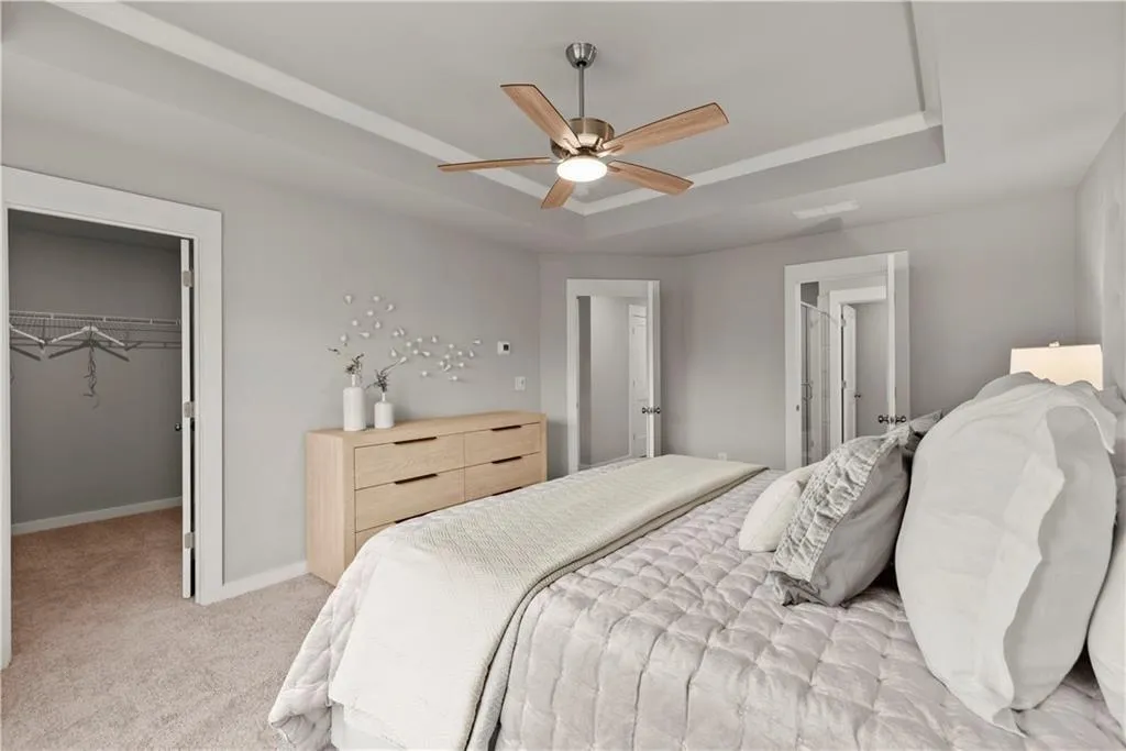 Bedroom with a raised ceiling, a spacious closet, light colored carpet, and a ceiling fan