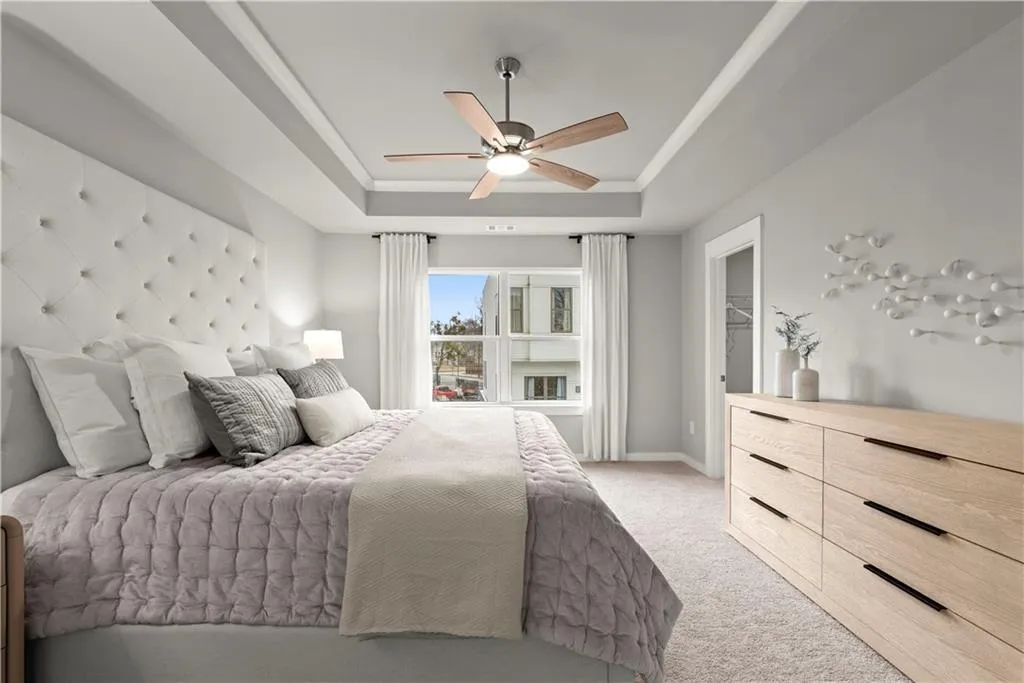 Bedroom featuring light carpet, a tray ceiling, and ceiling fan