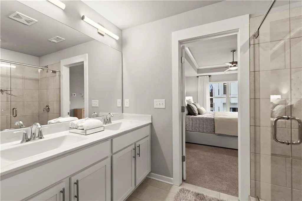 Ensuite bathroom with double vanity, a stall shower, light tile patterned floors, and ceiling fan