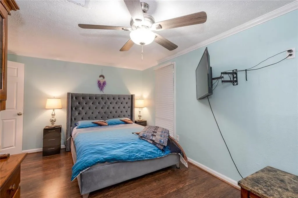 Bedroom featuring a textured ornamental molding, dark wood-type flooring, and ceiling fan, Mounted TV Stays with Home