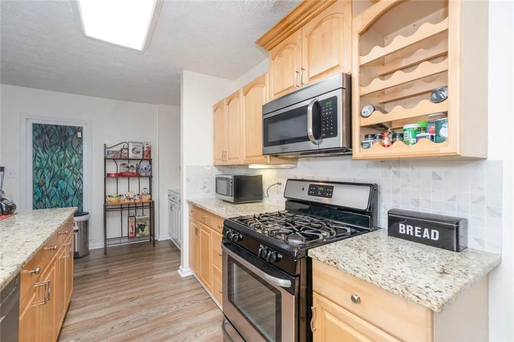 Kitchen featuring stainless steel appliances, light stone counters, light hardwood / wood-style floors, and light brown cabinets