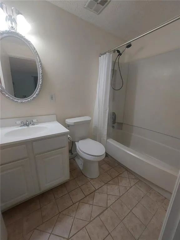 Full bathroom with vanity, shower / bath combo with shower curtain, toilet, and tile patterned flooring