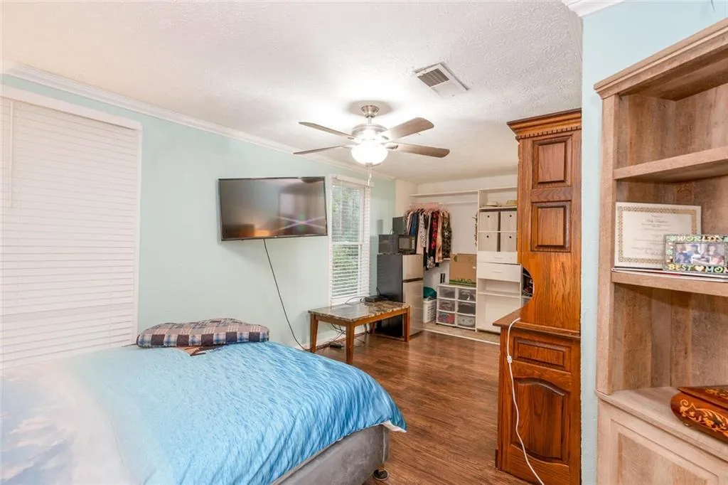Bedroom with dark wood-type flooring, a closet, a ceiling fan, and ornamental molding