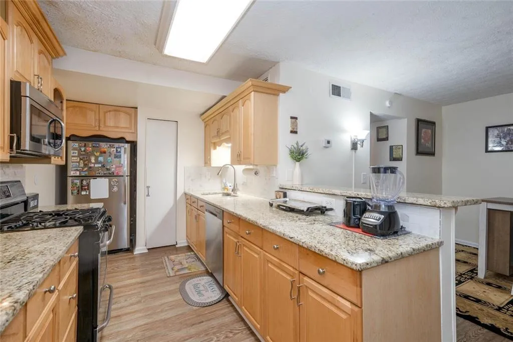 Kitchen featuring light stone counters, kitchen peninsula, light hardwood / wood-style flooring, stainless steel appliances, and light brown cabinetry