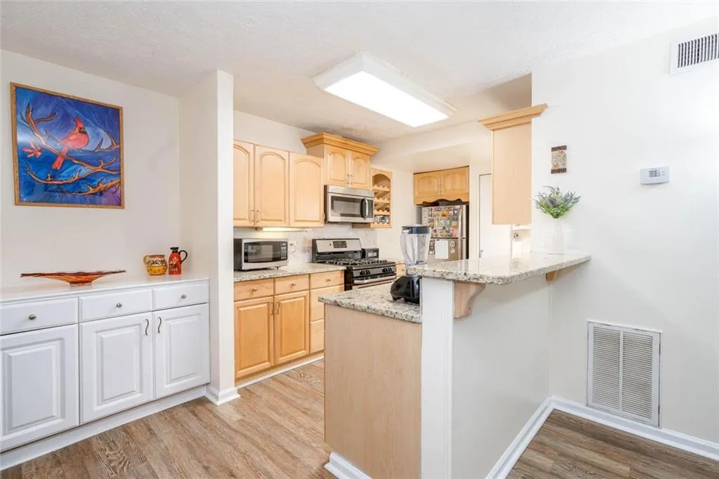 Kitchen with light wood-type flooring, kitchen peninsula, appliances with stainless steel finishes, and light brown cabinetry