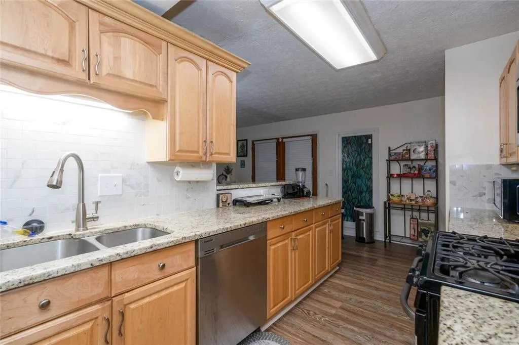 Kitchen with black range with gas stovetop, light stone counters, dishwasher, dark hardwood / wood-style floors, and sink