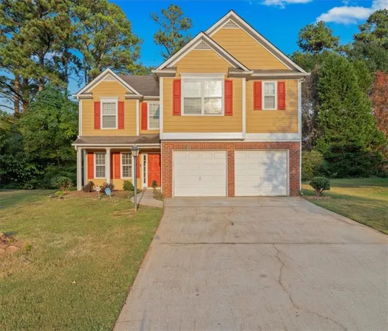 Two-story residence featuring a mustard yellow exterior with red shutters, a brick foundation, and a two-car garage
