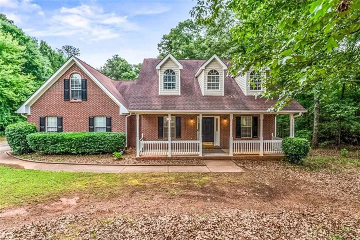 Traditional brick exterior featuring a covered porch with white railings, dormer windows, and mature perimeter trees