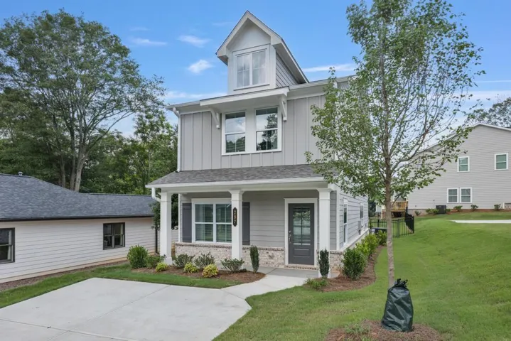Two-story residence featuring light gray siding with board and batten accents, a stone veneer foundation, and a covered front porch with white columns