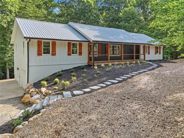 White vertical siding exterior with wood shutters, a metal roof, and a covered porch