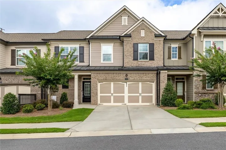Multi-story townhome featuring a brick and siding exterior, a two-car garage with carriage-style doors, a covered front entry with columns, and mature landscaping